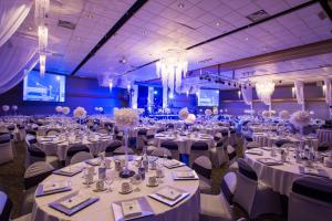 um salão de banquetes com mesas e cadeiras brancas e lustres em Le Noranda Hotel & Spa, Ascend Hotel Collection em Rouyn