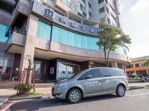 een zilveren busje geparkeerd voor een gebouw bij Jiuwu Hotel in Luodong