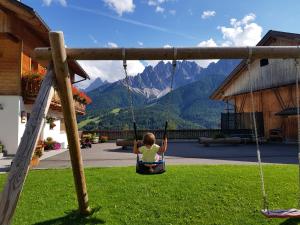 una niña sentada en un columpio en un patio en Ferienwohnungen Kuentnerhof en San Candido