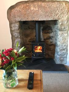 uma lareira com um vaso de flores e um controlo remoto em The Stopping Point- Exceptional Cumbrian Cottage em Flookburgh