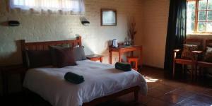a bedroom with a bed and a table and a window at Old Transvaal Inn Accommodation in Dullstroom
