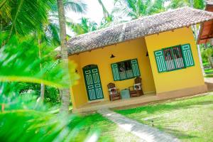 a yellow house with two chairs and palm trees at Kurumba Villas in Bentota