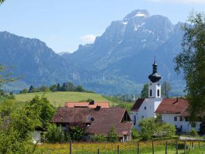 a small white church with a steeple with mountains in the background at Gasthof Rössle in Rieden am Forggensee