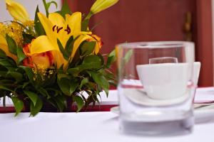 a glass sitting on a table with a vase of flowers at Penzión Donet in Bratislava
