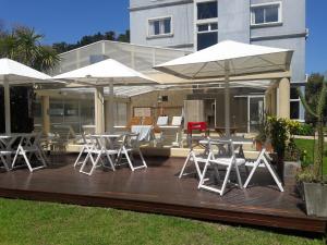 una terraza con mesas, sillas y sombrillas blancas en Casa Celeste en Valeria del Mar