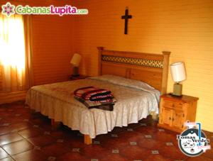1 dormitorio con 1 cama y 1 cruz en la pared en Cabañas Lupita 31, en Mazamitla