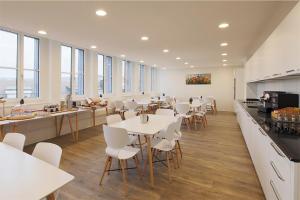 a cafeteria with white tables and chairs and windows at Hotel Work Life Residence am Bahnhof in Winterthur