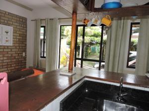 uma cozinha com um balcão com um lavatório e janelas em Pousada Beija-Flor em Bombinhas