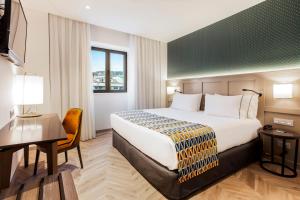グラナダにあるEurostars Puerta Realの大きなベッドと机があるホテルの部屋