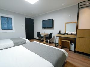 a hotel room with two beds and a desk and a television at Hotel Tong Yeondong Jeju in Jeju