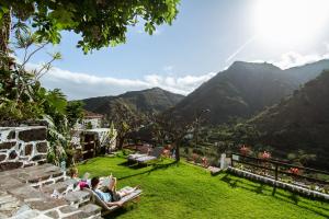 eine Gruppe von Menschen, die auf dem Rasen mit Bergen sitzen in der Unterkunft Apartamentos Los Telares in Hermigua