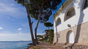 a building with a tree next to a body of water at ALCUDIA-VIDA SANA-PRIMERA LINEA DE MAR in Alcudia