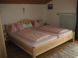 uma cama de madeira com almofadas cor-de-rosa e uma cruz na parede em Gästehaus Proisl em Lenggries