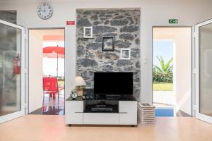 a living room with a tv and a stone wall at Casa Sol e Vista in Arco da Calheta