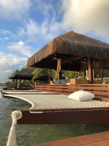een resort op het water met stoelen en een rieten dak bij Casa praia Porto de Galinhas Toquinho in Ipojuca