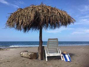 una silla sentada bajo una sombrilla de paja en la playa en Villa del Mar, en Costa Esmeralda