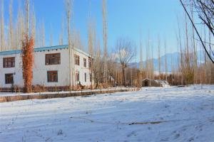 a white building in a snowy field with trees at amir homestay in Leh