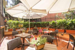 un patio con mesas, sillas y una sombrilla en Hotel Espana - Gruppo BLAM HOTELS en Roma