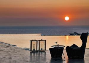 a sunset over the ocean with a table and chairs at Santo Pure Oia Suites & Villas in Oia