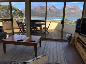 a living room with a table and a balcony with mountains at Freycinet Beach House in Coles Bay