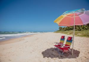 twee stoelen en een parasol op een strand bij Flat Guarajuba Beira da Praia pé na areia in Guarajuba