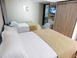 a hotel room with two beds and a television at Flats Ouro Gramado Localizado a 900 metros da entrada do Centro de Gramado in Gramado