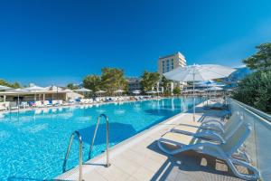 a large swimming pool with chairs and an umbrella at Bluesun Holiday Village Alan in Starigrad