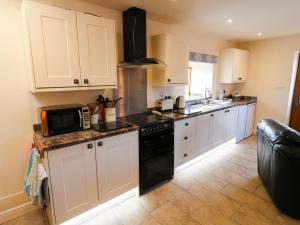 uma cozinha com armários brancos e um forno de fogão preto em The Stables em Parwich