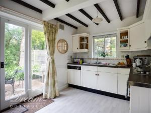 cocina con armarios blancos y ventana grande en Little Berwick Cottage en Burton Bradstock