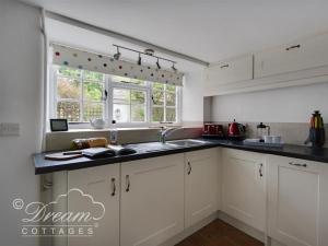 a kitchen with white cabinets and a sink and a window at Bramble Cottage in Burton Bradstock