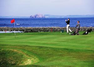 dos personas jugando golf en un campo de golf junto al océano en Duck's Inn, en Aberlady