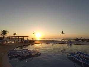 una piscina con sillas y una puesta de sol en el fondo en Golden Lake - FLX Pé na Areia 1 ARRAIAL DO CABO, en Arraial do Cabo