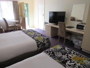 a hotel room with two beds and a desk with a television at Moruya Motel in Moruya