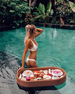 a woman in a bikini in the water with a tray of food at Honai Resort in Ubud