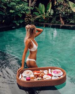 una mujer en bikini en el agua con una bandeja de comida en Honai Resort, en Ubud