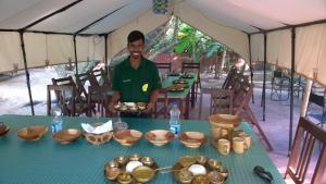 mężczyzna stojący w namiocie ze stołem z jedzeniem w obiekcie Nature Camp Konark Retreat w mieście Konark