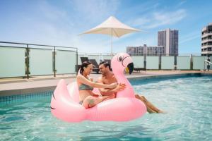 un homme et une femme assis sur un flamingo rose dans une piscine dans l'établissement voco Gold Coast, an IHG Hotel, à Gold Coast