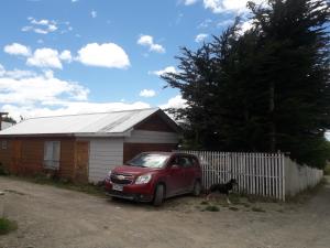 um carro vermelho estacionado em frente a uma casa com um cão em Casa de Campo A Pasos De La Ciudad em Punta Arenas