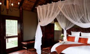 1 dormitorio con cama con dosel y almohadas de color naranja y blanco en Zwahili Private Game Lodge & Spa, en Modimolle
