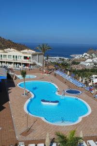 a large swimming pool with chairs and the ocean at Apartamentos Natural Park in Puerto Rico de Gran Canaria