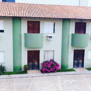 a white building with green columns and pink flowers at Casinha no Sal - Tangaroa Residencial in Salinópolis