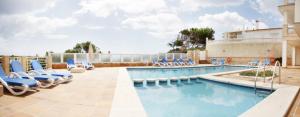 a swimming pool with blue lounge chairs and a pool at Apartamentos Villa Sirena in Cala Figuera