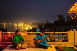 Dois homens estão sentados num parapeito a tocar guitarra. em Wander Station Varanasi em Varanasi