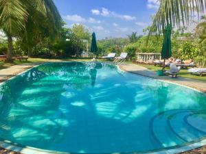 a large blue swimming pool with people sitting on chairs in a yard at Asian Jewel Boutique Hotel in Hikkaduwa