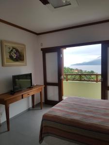 1 dormitorio con 1 cama, TV y ventana en Bangalô com vista para o mar no condomínio Yacamim Ilhabela praia do Curral, en Ilhabela