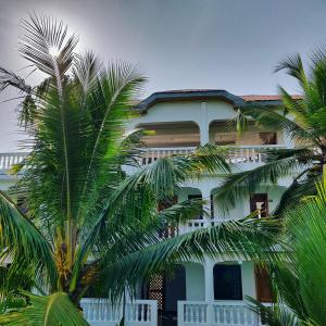 a white building with palm trees in front of it at Laughing Goat Ghana Hostel in Busua