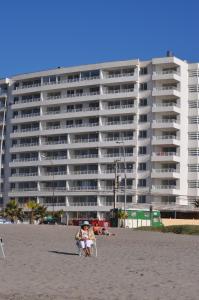 a woman sitting in a chair on the beach in front of a building at Departamento frente al mar in La Serena