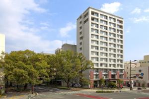 a tall white building on a city street with trees at K's Street Hotel Miyazaki in Miyazaki