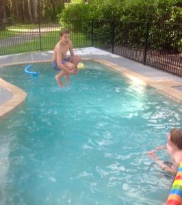 a boy jumping into a swimming pool with a frisbee at Mistinthegumtrees Eco Luxury Cabins in Cooranbong
