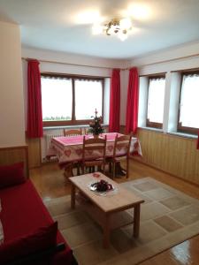 sala de estar con mesa y cortinas rojas en Appartamenti Riz Claudio, en Campitello di Fassa